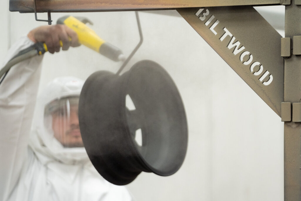 Biltwood Powder Coating technician applying a black powder coat to a metal rim inside the spray booth.