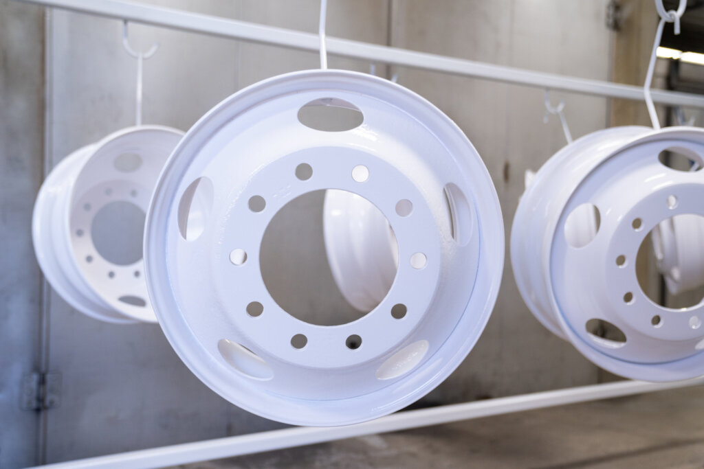 White powder-coated metal rims hanging on a conveyor system at Biltwood Powder Coating facility.